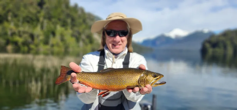 Pescador con una trucha fontinalis en el lago Fonck, con montañas de Patagonia al fondo