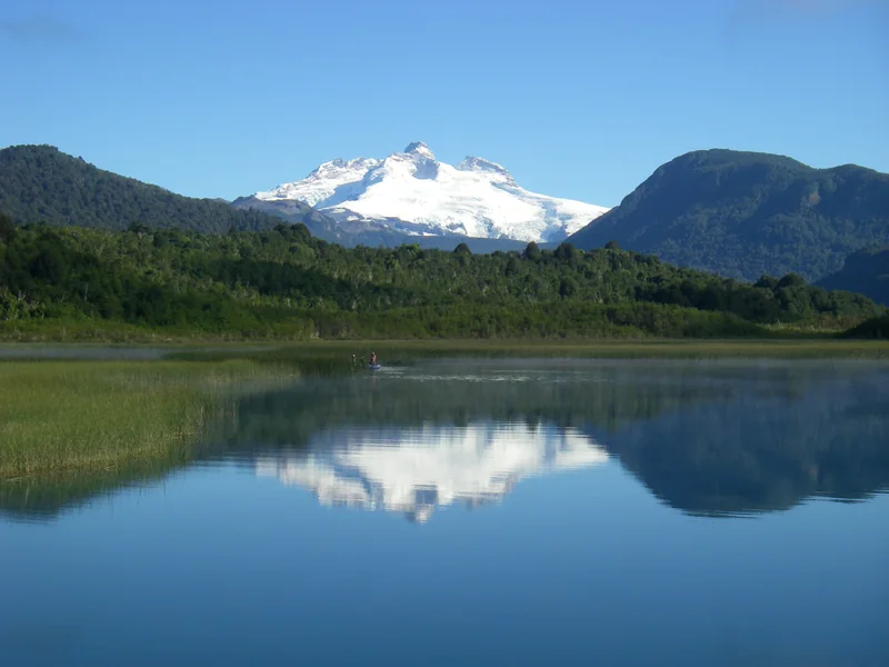 Montañas nevadas reflejadas en el lago Hess junto a una balsa de pesca en Patagonia