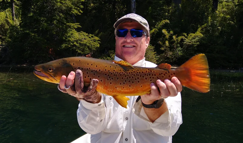 Pescador con una trucha marrón en el lago Roca, rodeado de bosque patagónico