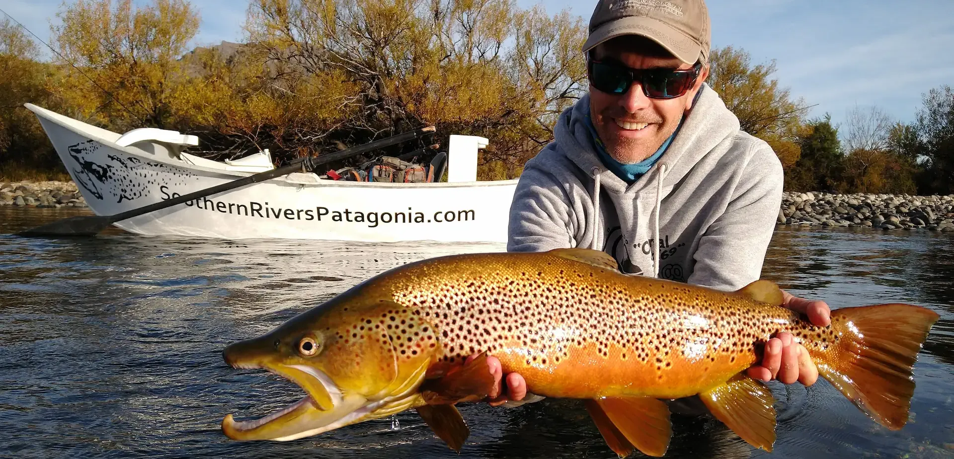 Fly fisherman holding a large migratory brown trout on the Limay River in Bariloche, Patagonia, Argentina.