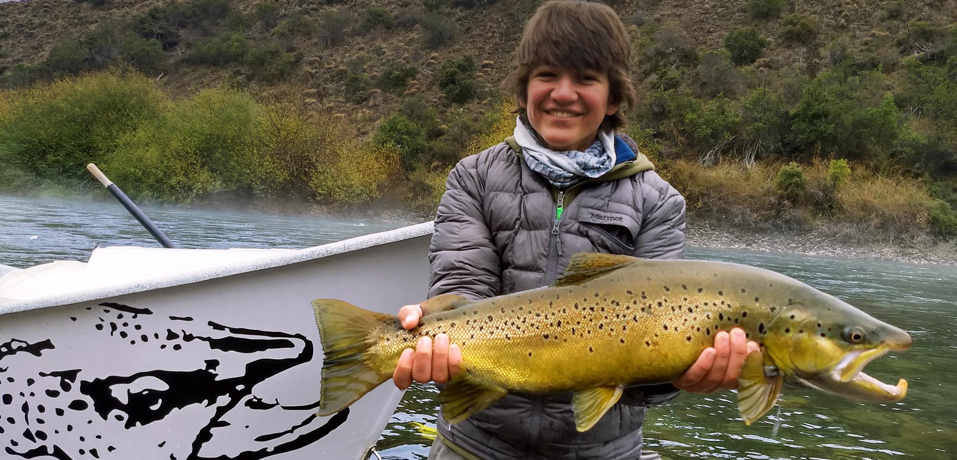 Young fisherman holding a fish in his hand while fly fishing in the river in Bariloche, Argentina, a popular destination for sport fishing in Patagonia.